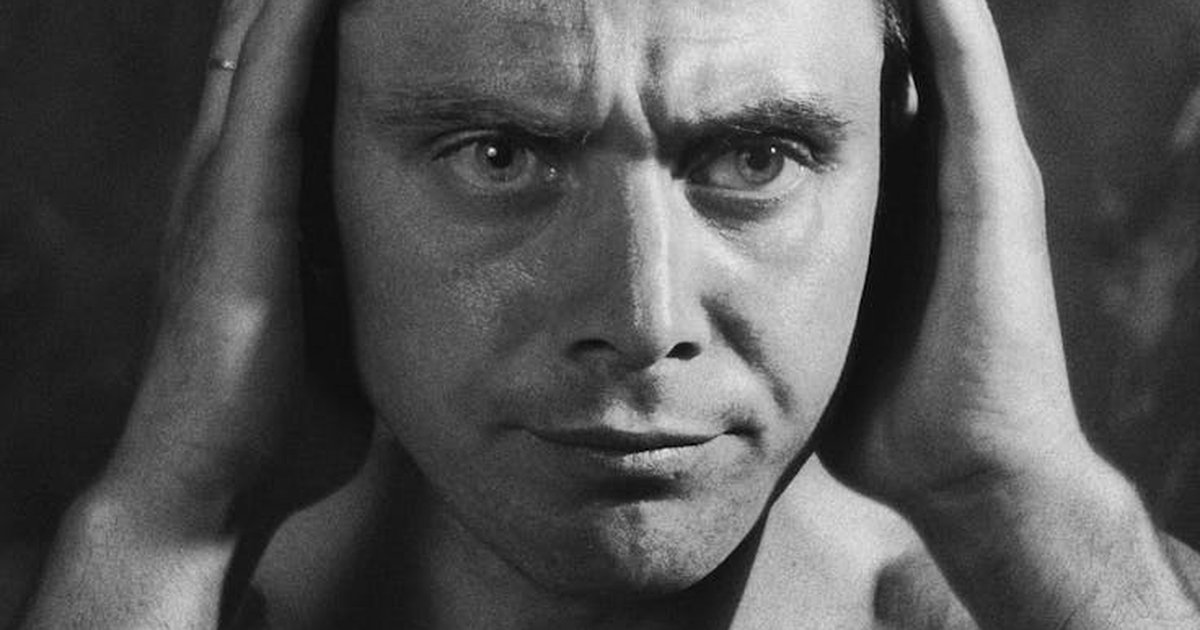 Close-up grayscale portrait of a serious man with hands to head, highlighting emotional intensity.