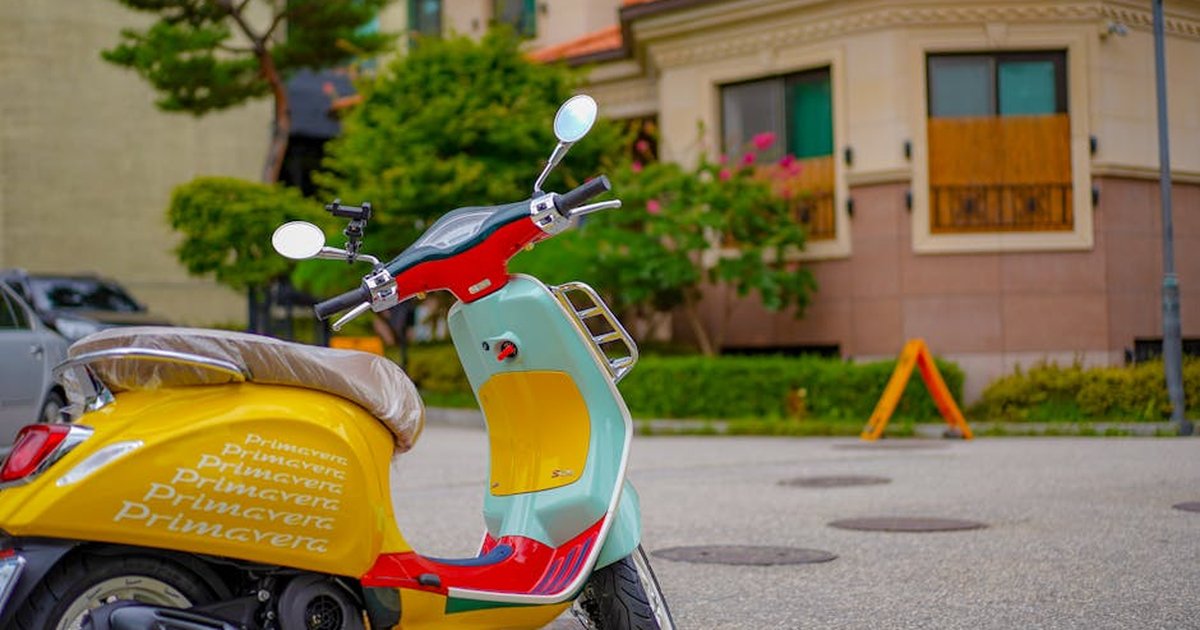 A vibrant, stylish Vespa scooter parked in a residential urban setting.