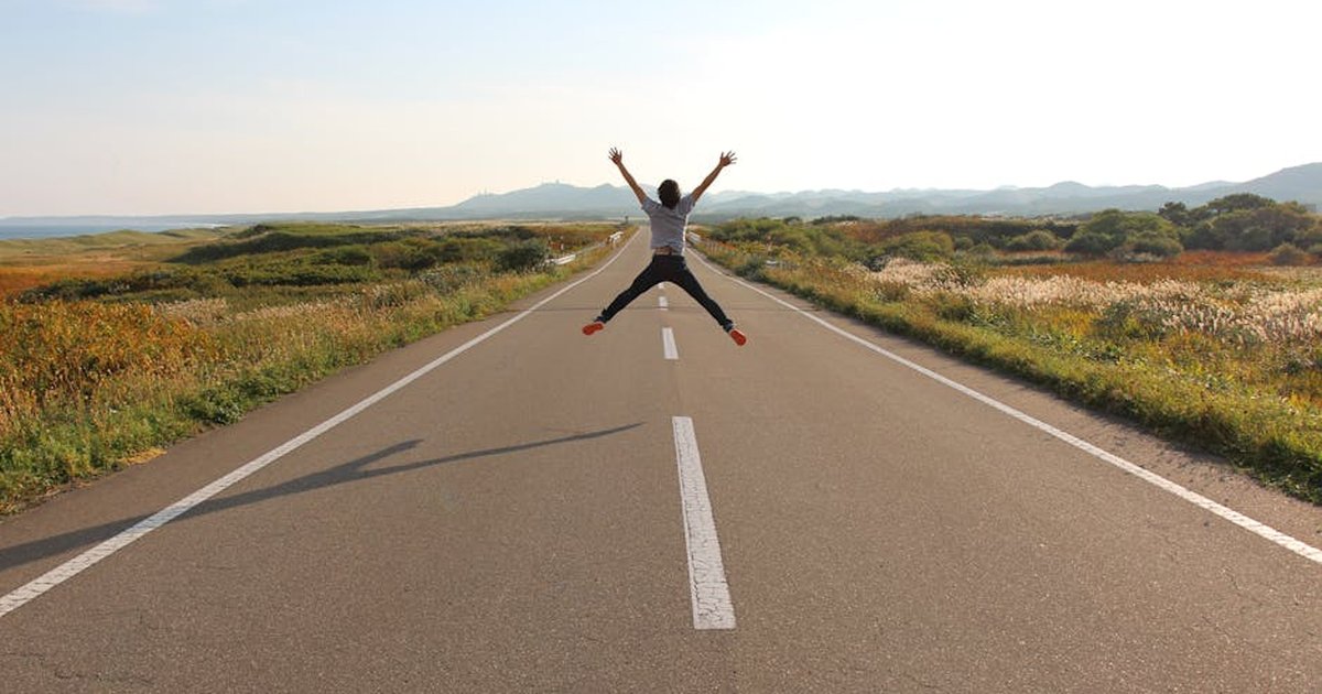 Person jumping on an open road in Hokkaido's scenic landscape on a sunny day.