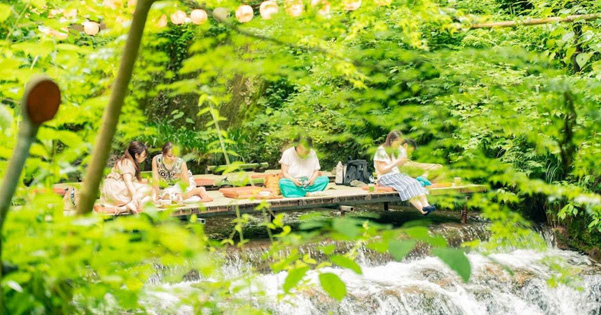 Group enjoying a serene kawadoko setting by a stream in lush Kyoto, Japan.