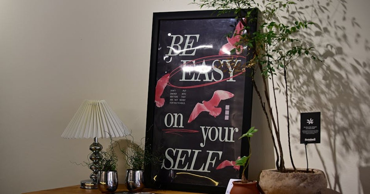 Stylish wall art with motivational text alongside a table with plants and lamp.