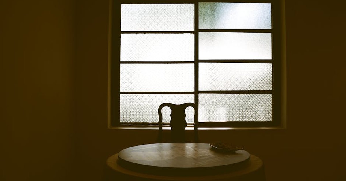 A vintage setup with a chair and round table silhouetted against a textured window.