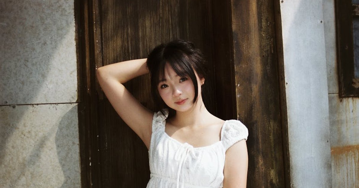 A young woman poses in a white dress against a rustic wooden door, evoking a serene summer day.