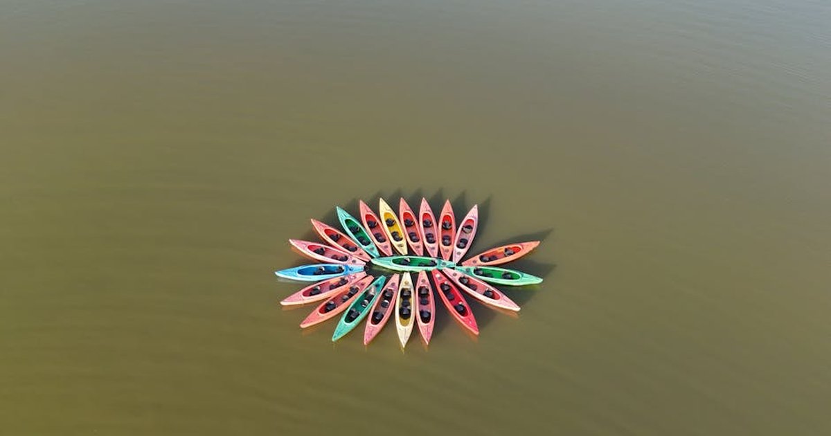Drone view of multicolored kayaks forming a circle on calm lake waters.