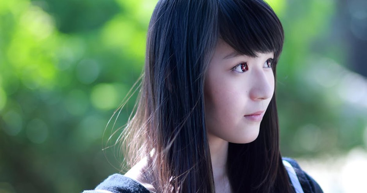 Close-up portrait of a young woman with long hair outdoors. Soft lighting and green background.