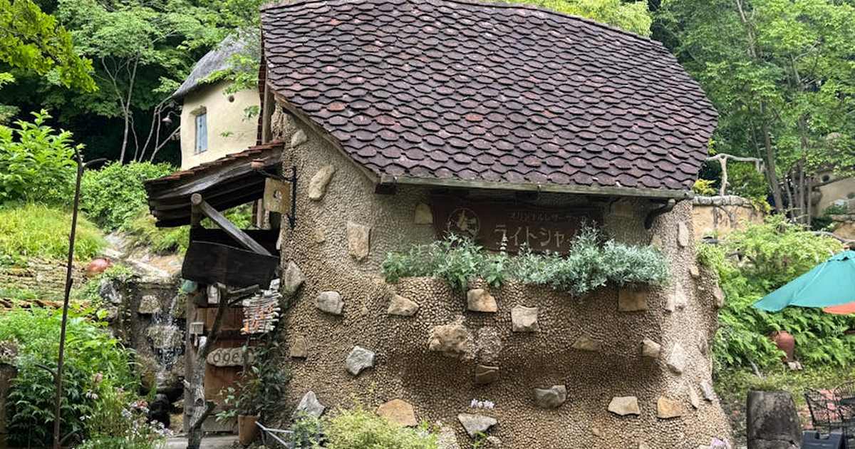 A charming rustic cafe with stone walls and a thatched roof nestled in a lush green forest.