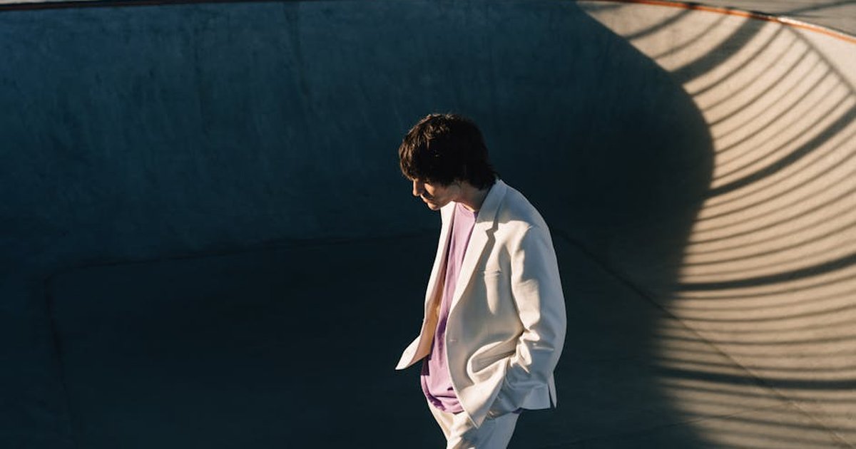 Fashionable man in white blazer walking in a sunlit skate park bowl.
