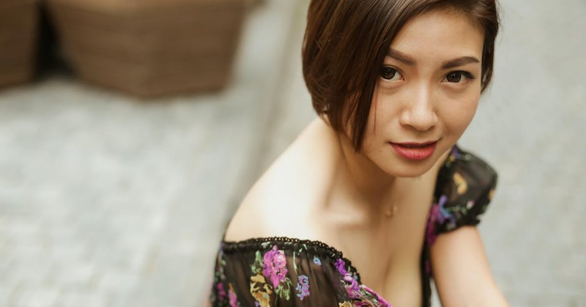 A portrait of a woman in a floral dress sitting outdoors with a soft focus background.