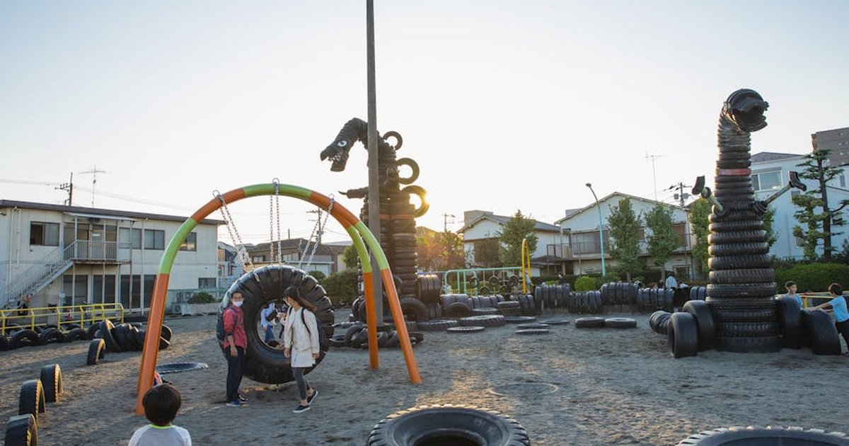 Small yard with huge monster creature figures constructed of old tyres on playground full of children