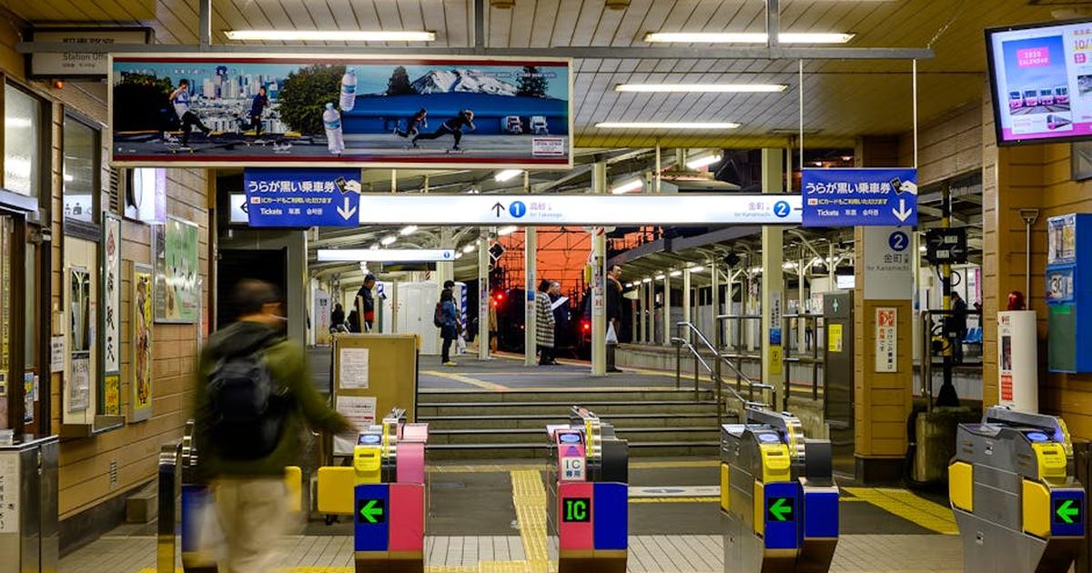 A busy evening scene at a Japanese train station featuring ticket gates and passengers entering the platform area.
