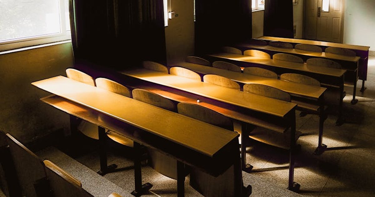 Sunlight streaming into an empty classroom with wooden desks and chairs in Hubei, China.