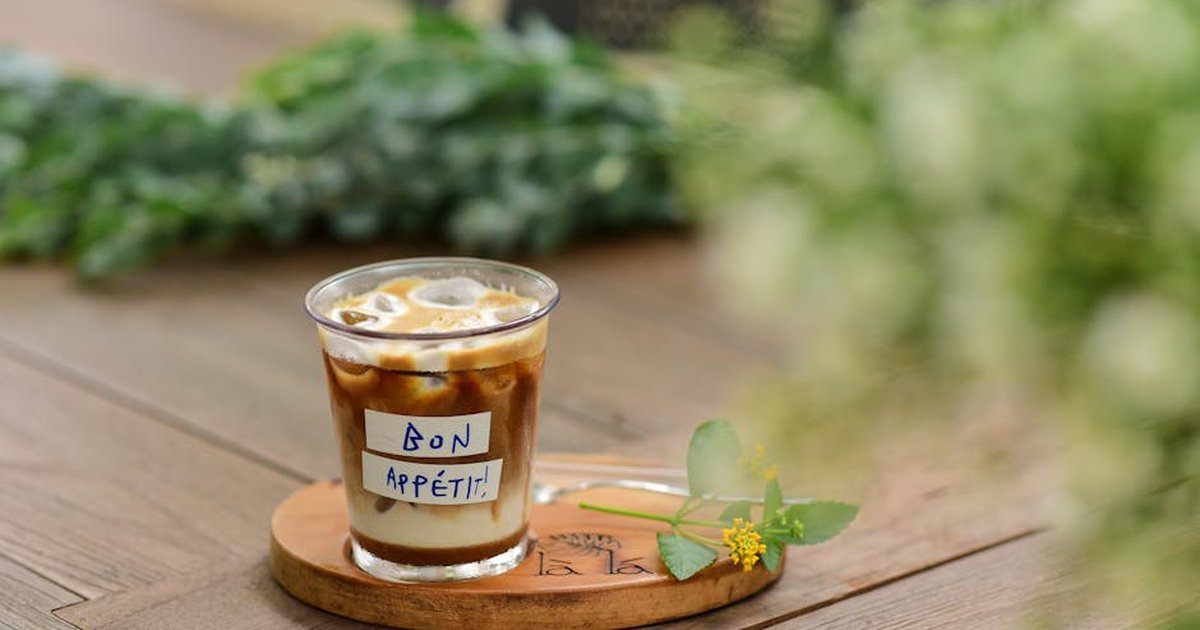 Iced coffee with a 'Bon Appétit' note on a wooden table, with floral decor.