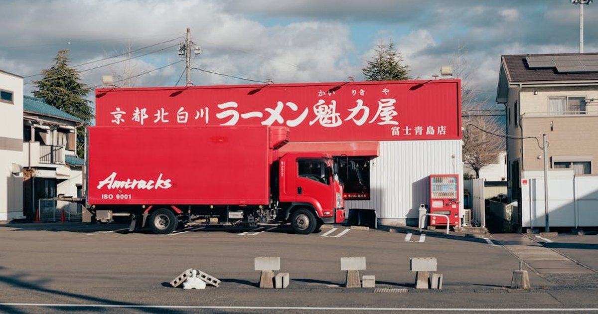 Red delivery truck parked outside a ramen shop in Fuji, Japan, under blue skies.