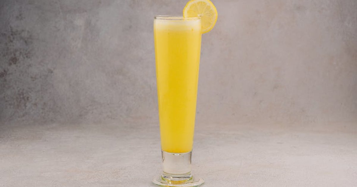 Tall glass of fresh lemon juice with a slice garnish on gray background.