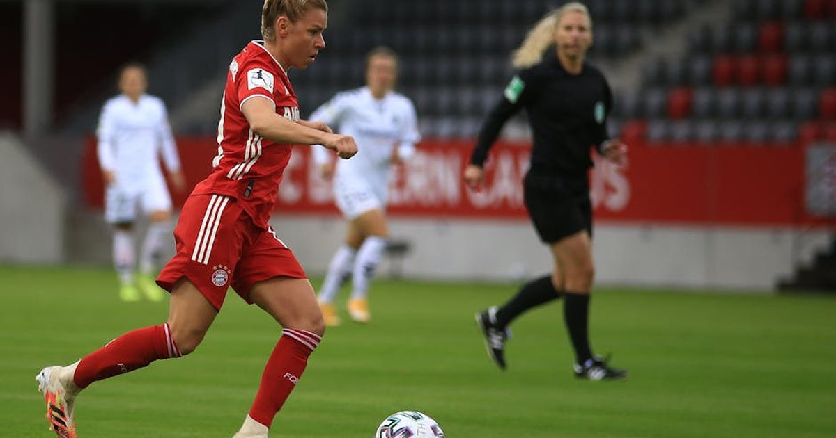 A female soccer player in red uniform dribbles during a match.