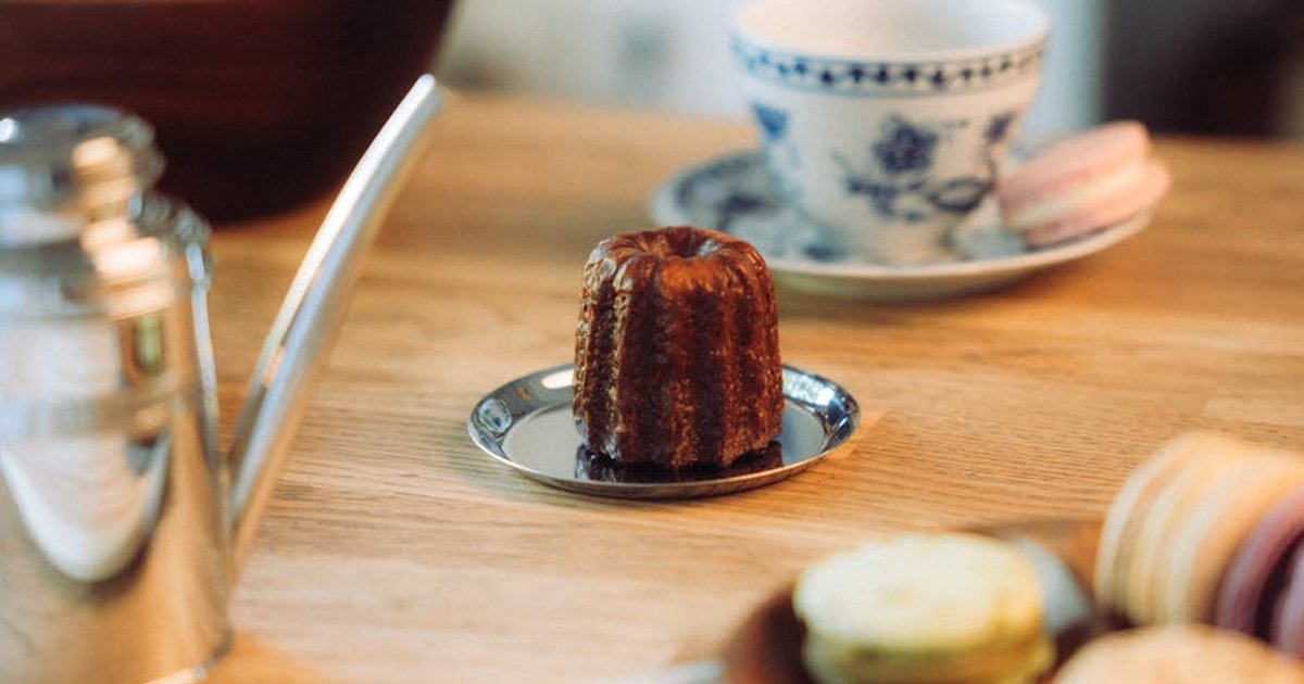 A cozy French patisserie setup featuring a canelé, macarons, and a tea set on a wooden table.