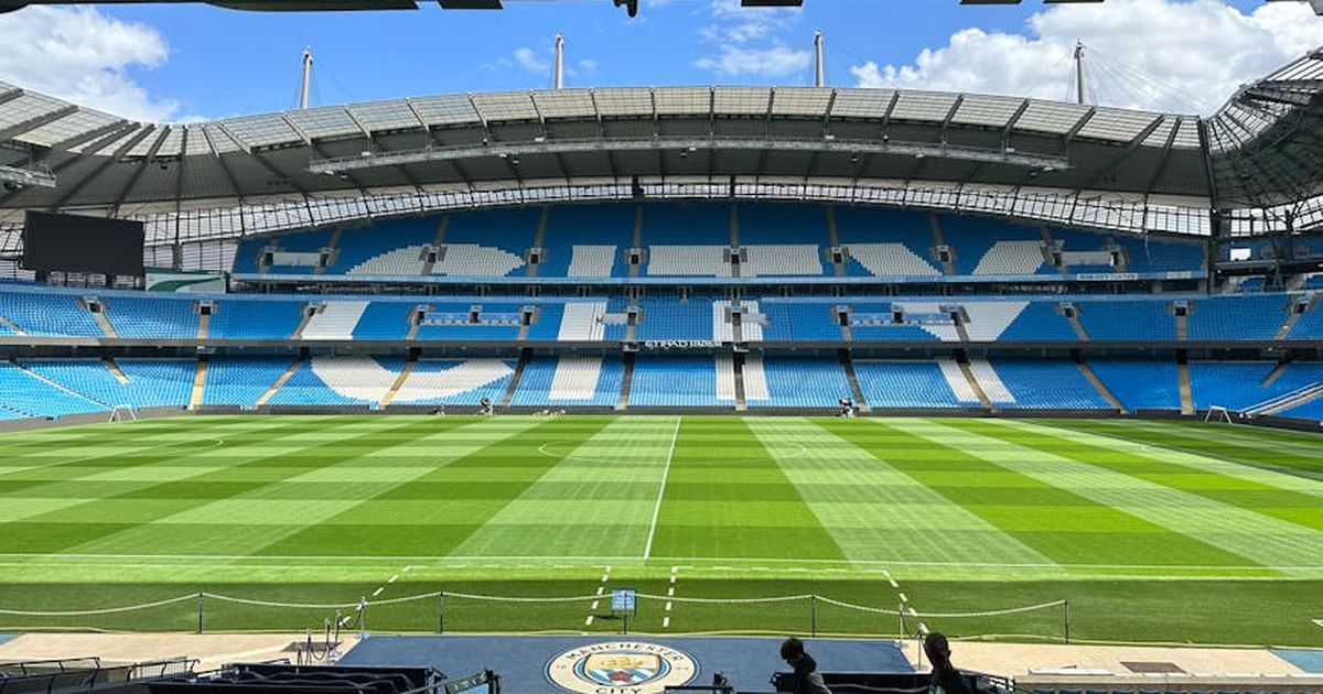 Panoramic view of Etihad Stadium, showcasing the empty football pitch and stands under a clear blue sky.