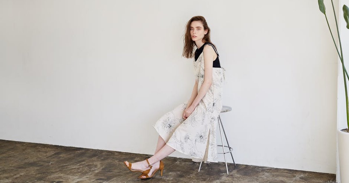 An elegant woman in a floral dress sitting on a stool in a minimalist interior setting.