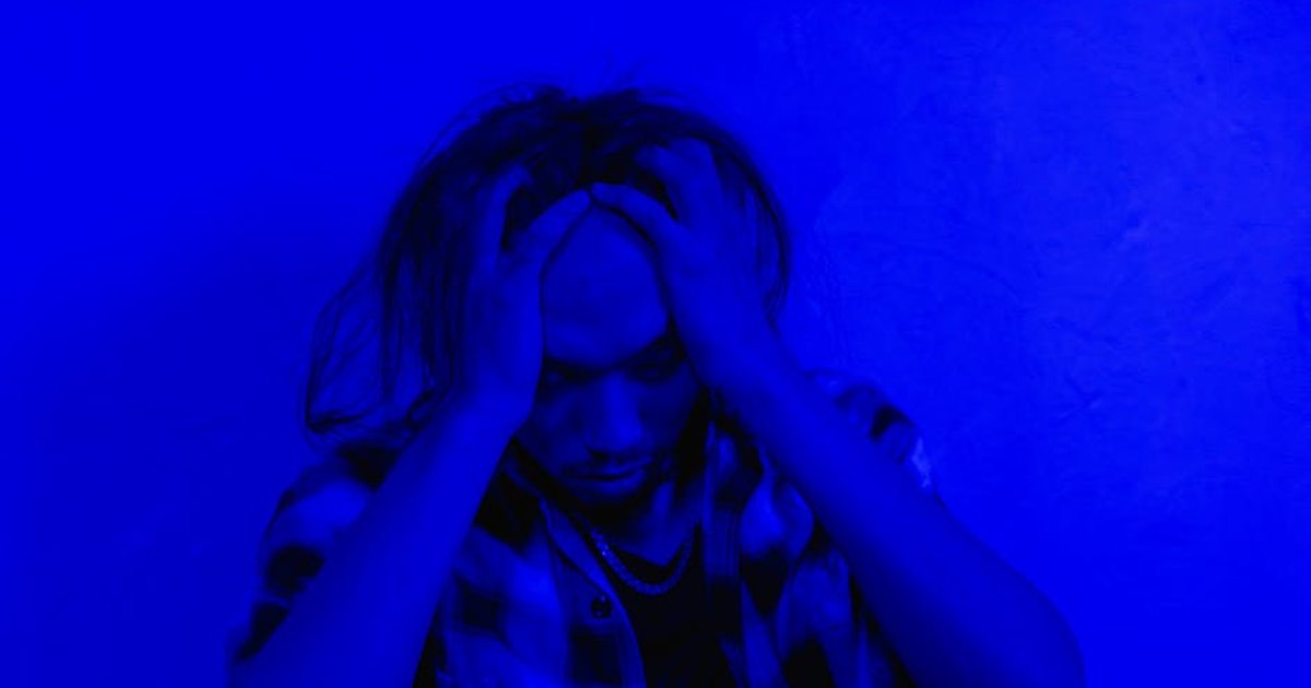 Portrait of a distressed person under dramatic blue lighting, expressing mental anguish.