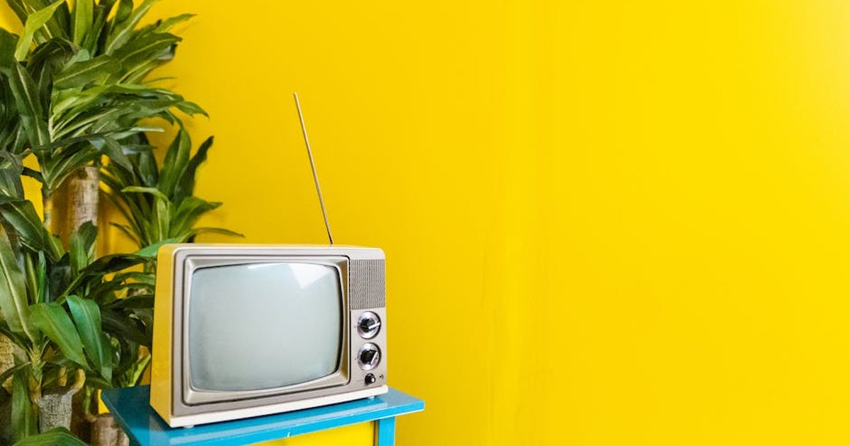 Retro TV sits on a blue table against a vibrant yellow wall, next to lush indoor plant.
