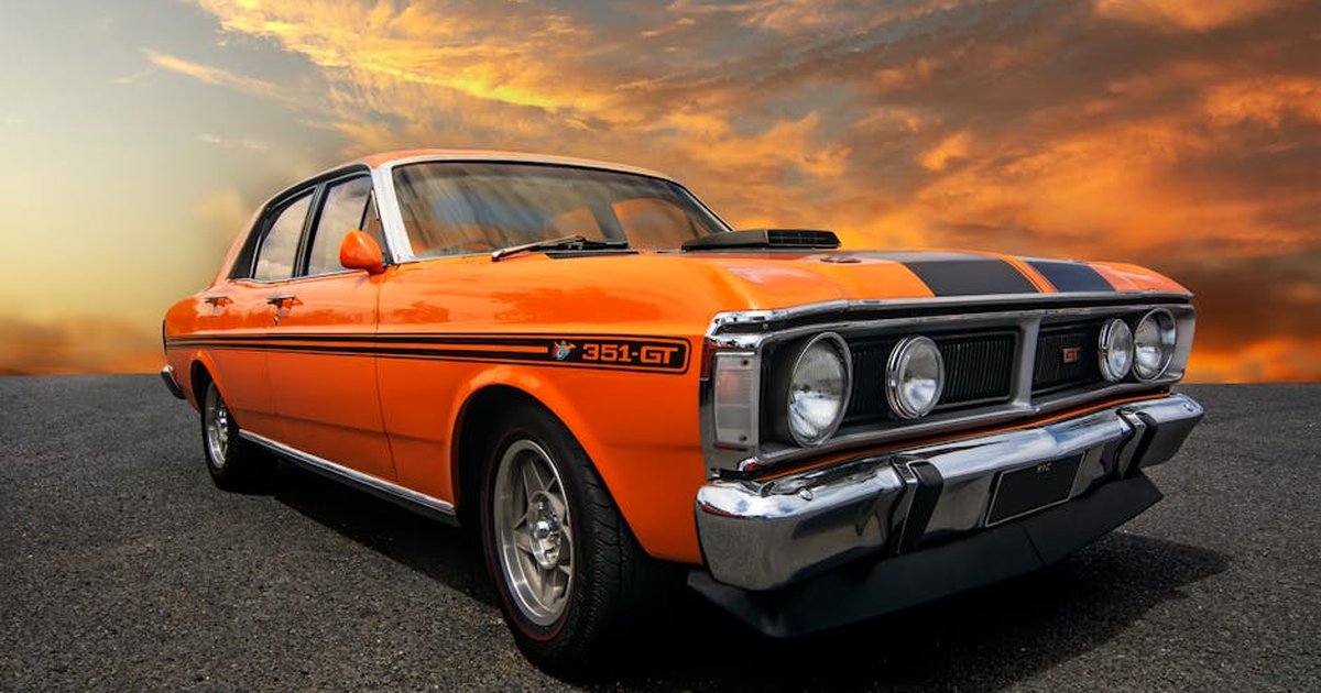 Vintage orange Ford Falcon 351 GT muscle car shining against a vibrant sunset sky.