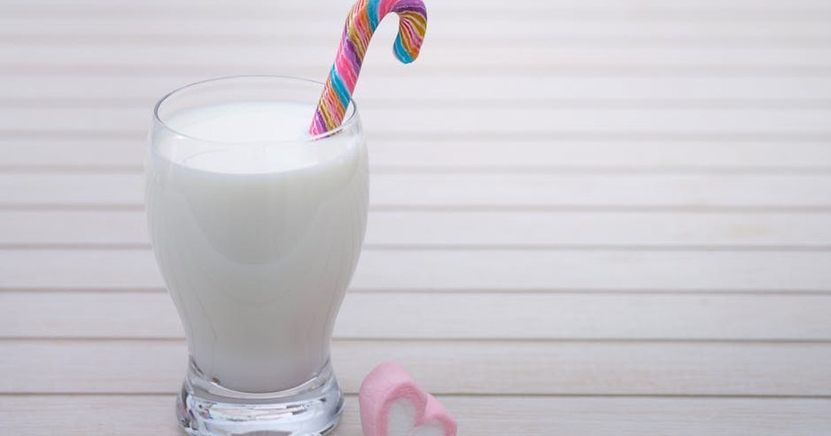 Glass of milk with a colorful candy cane and heart-shaped marshmallow on wooden table.