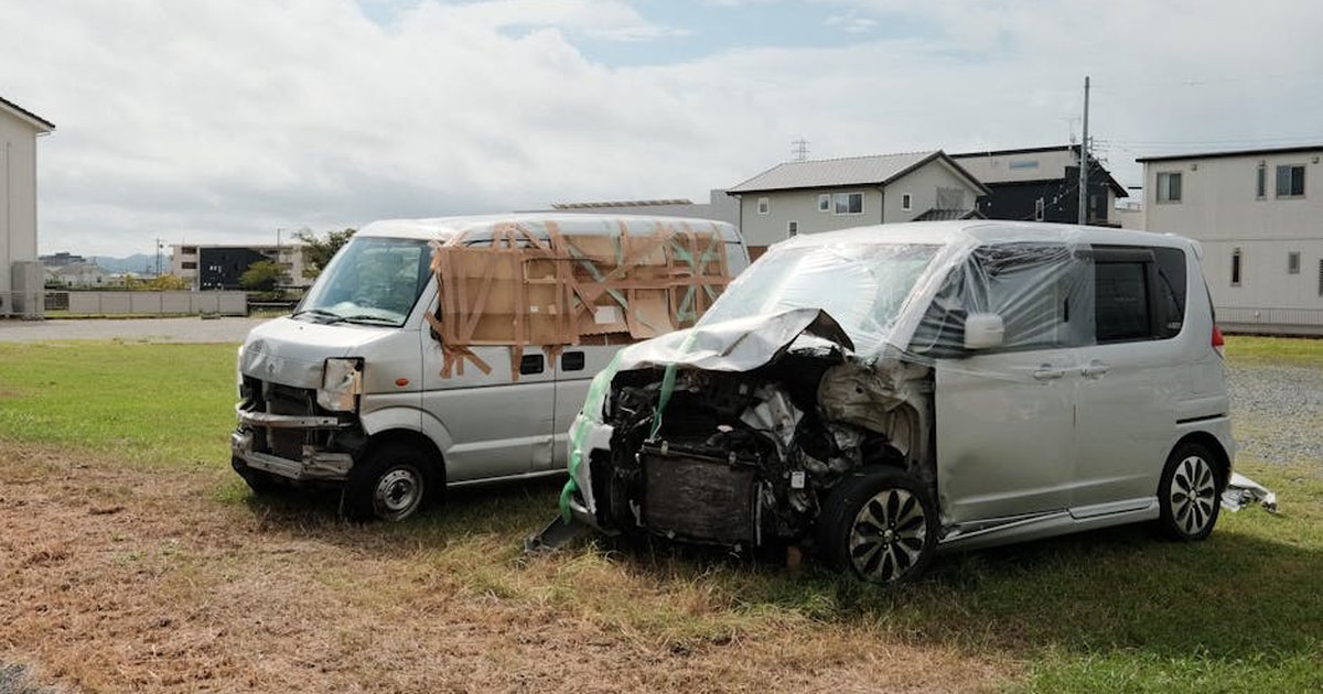 Two wrecked vans parked on a grassy area in Toyokawa, Japan.
