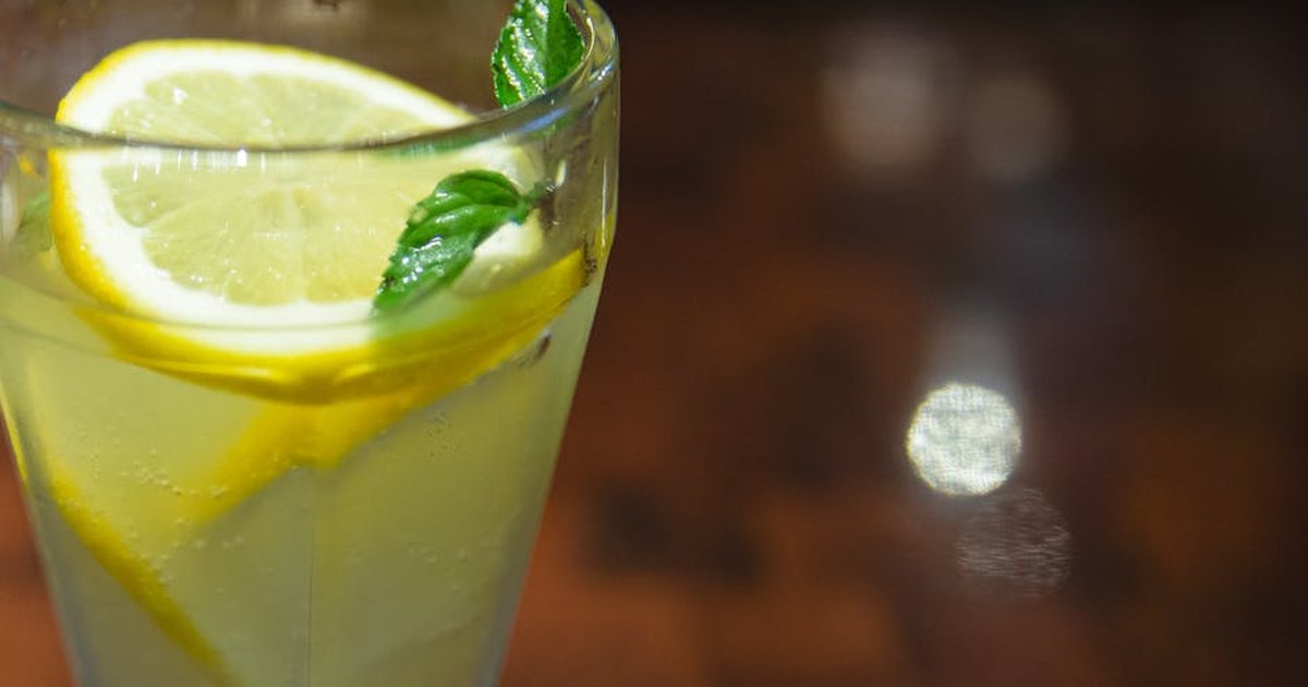 Glass of cold sour lemonade served with lemon slices and fresh mint leaf on blurred wooden table