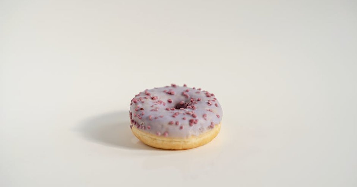 A close-up of a purple iced doughnut with red sprinkles on a plain white background.