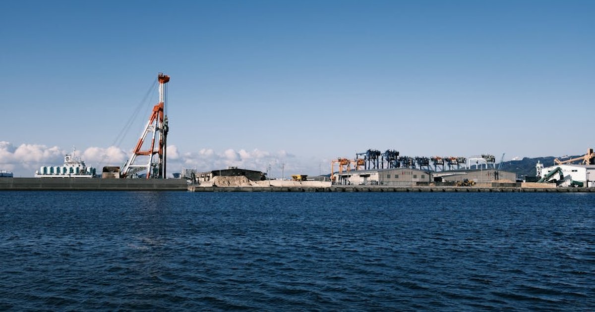 View of an industrial port in Gamagōri, Japan, showcasing cranes and the coastal area under a clear sky.