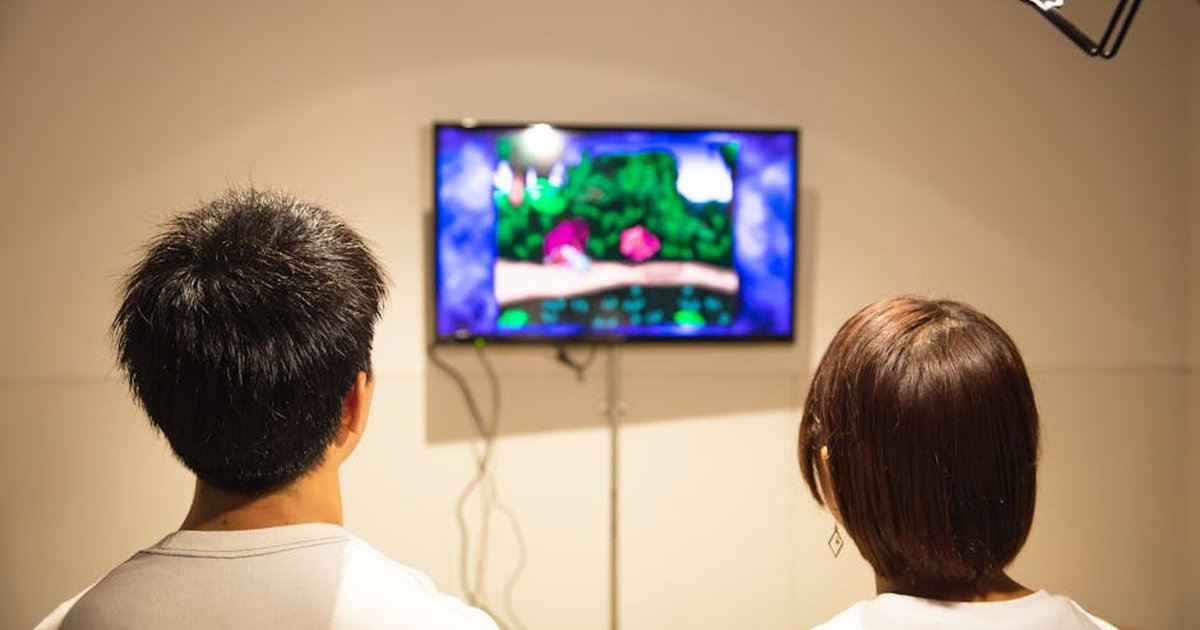 Back view of anonymous young guy and lady in white t shirts sitting in living room and playing video game