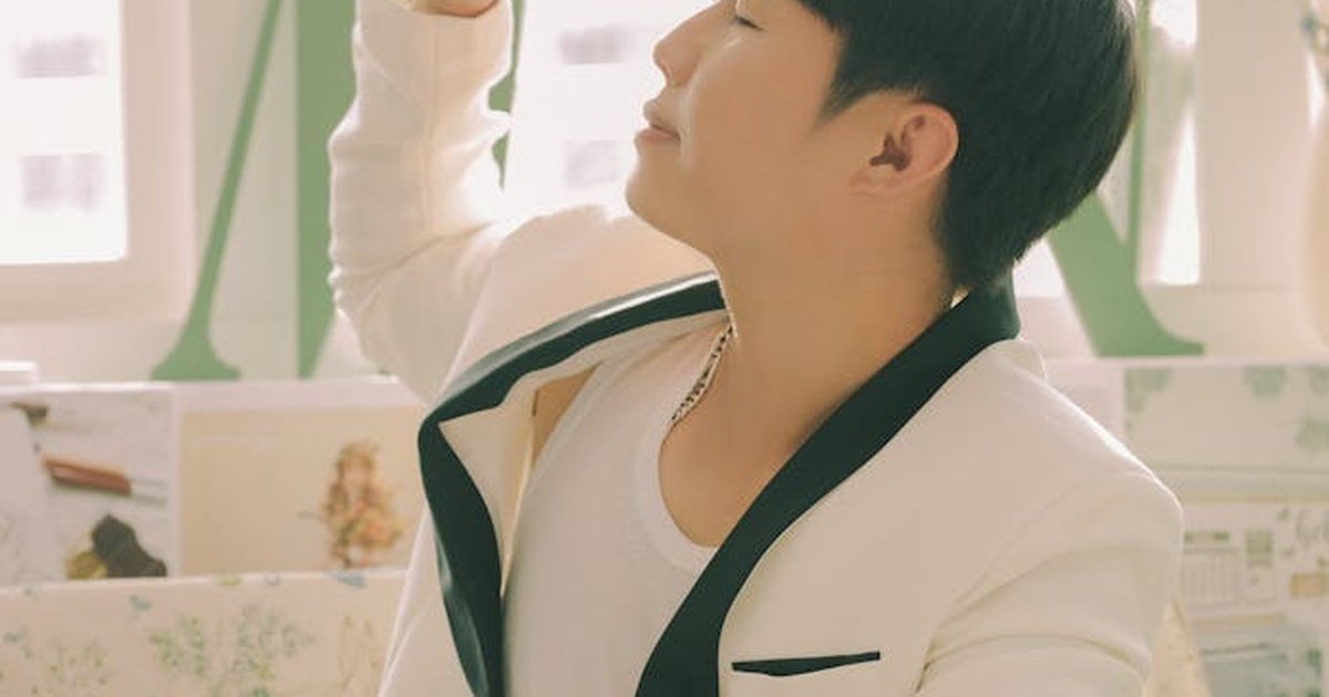 A young man in a chic white blazer enjoys sunlight indoors, exuding a relaxed vibe.