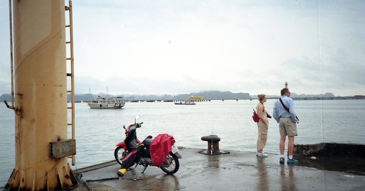 Couple stands on a pier at Ha Long Bay, Vietnam, with a ship in the distance.