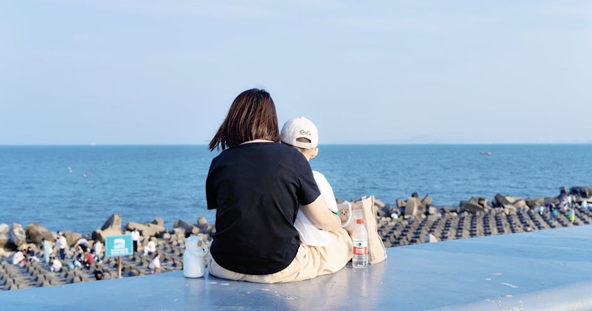 Mother and child sitting on seawall enjoying the ocean view.