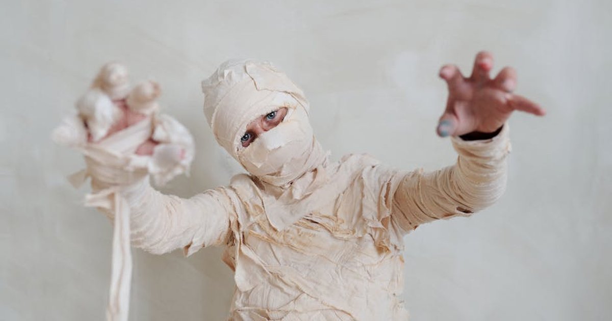 A child dressed as a mummy poses indoors for a spooky Halloween portrait.