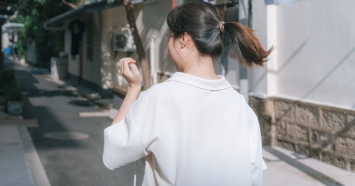 Young woman in a white blouse walking down a sunlit alley, capturing the essence of a summer day.