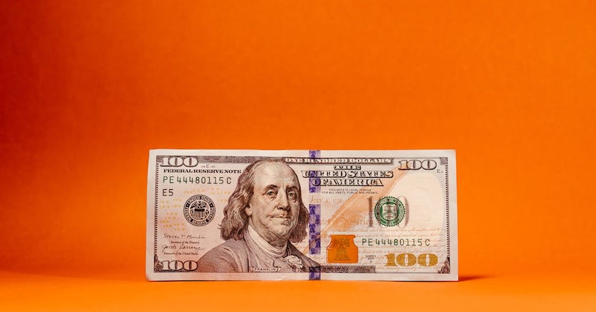 Crisp US hundred-dollar bill against a vivid orange backdrop. Ideal for finance themes.