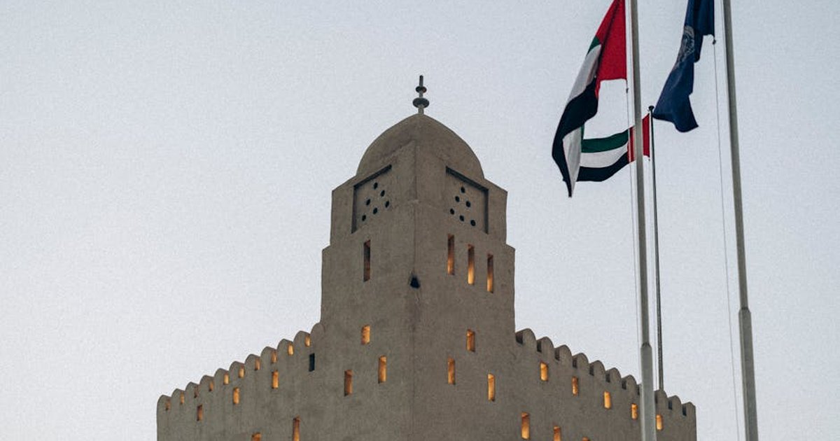 A traditional fortress with UAE flags at sunset in Abu Dhabi, showcasing architectural heritage.