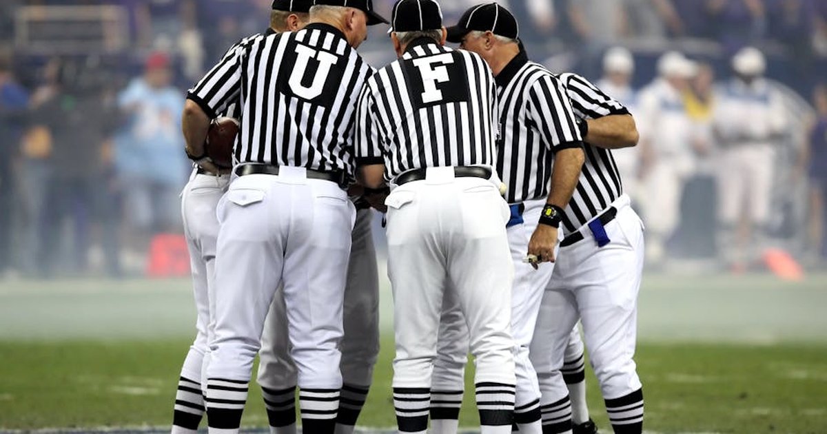 Group of sports officials in striped uniforms discussing on a football field.