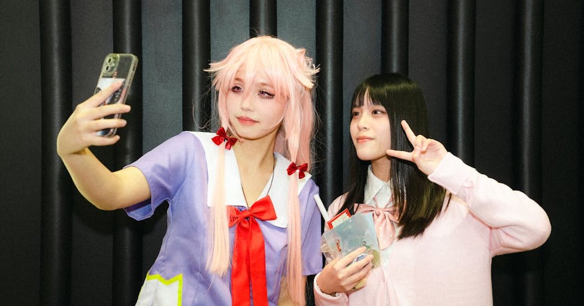 Two women in cosplay costumes taking a selfie indoors on a black background.