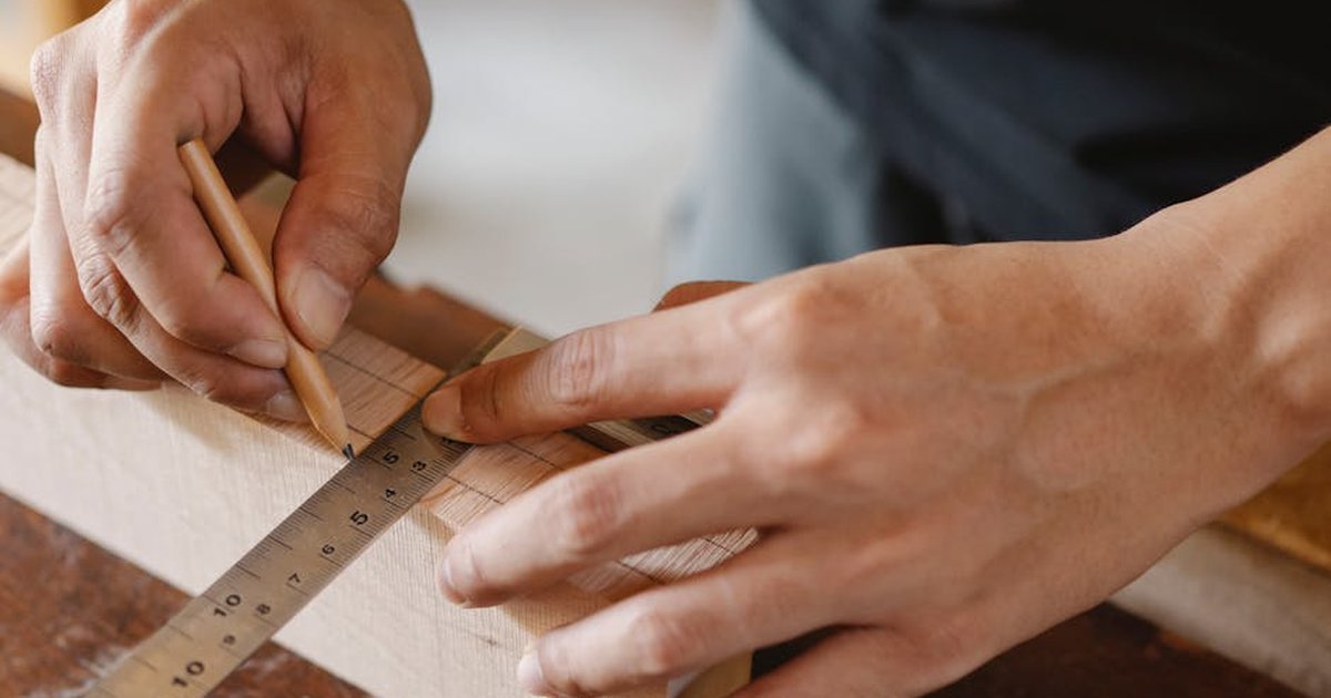 From above of crop anonymous male making lines with pencil on timber plank at table in workshop
