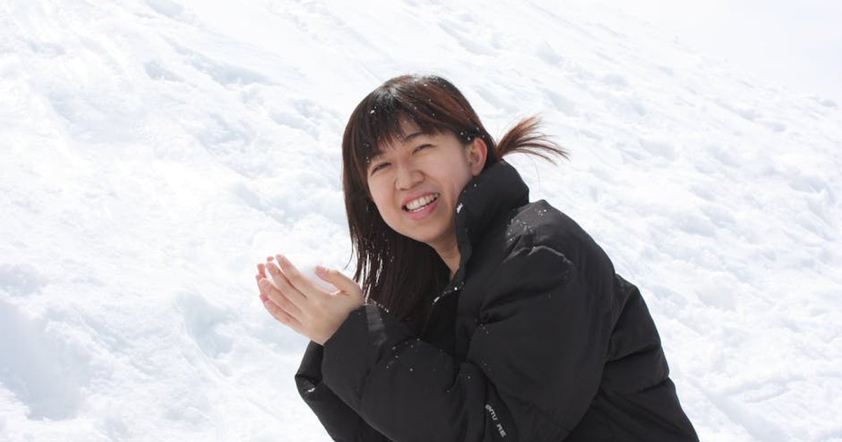 Smiling woman in black coat clapping hands in snowy landscape during winter day.