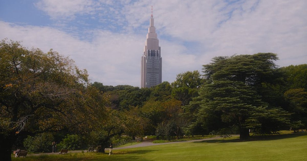 Serene view of Shinjuku Gyoen Park in Tokyo featuring the towering NTT Docomo Yoyogi Building under a bright sky.
