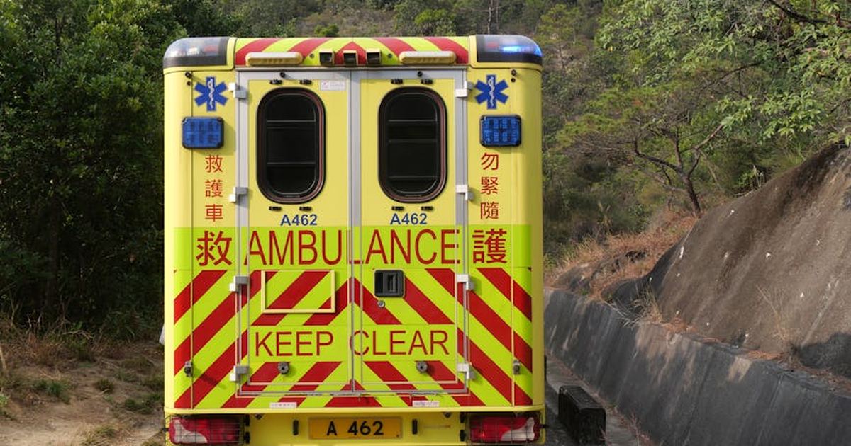 Back view of a Hong Kong ambulance on a narrow road surrounded by nature.