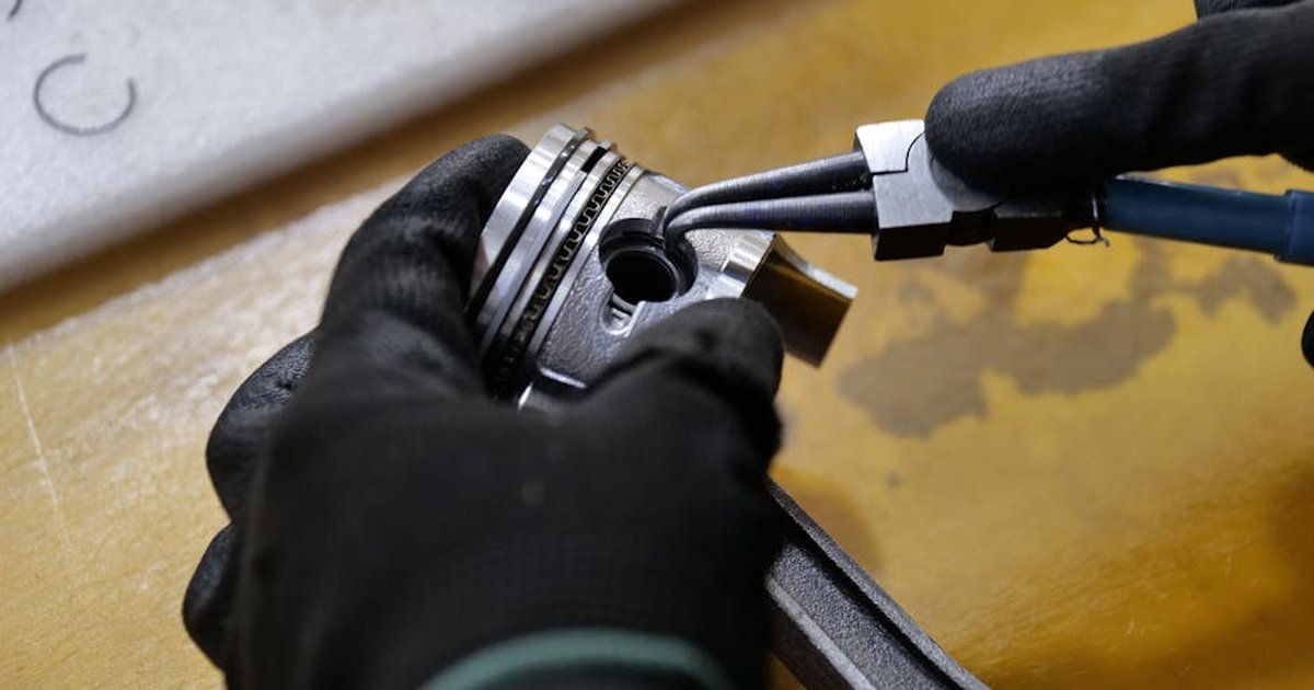 Gloved hands working on a piston rod in a workshop setting. Industrial repair scene.