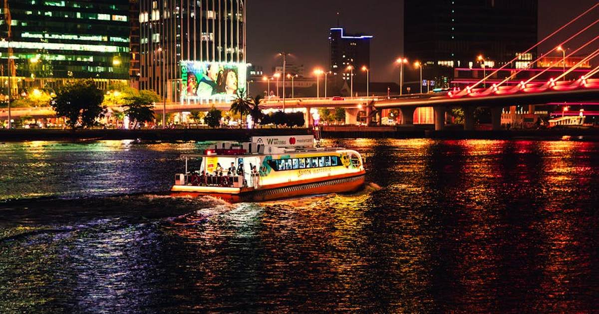 Illuminated boat cruises the Saigon River at night, showcasing Ho Chi Minh City's lively skyline.