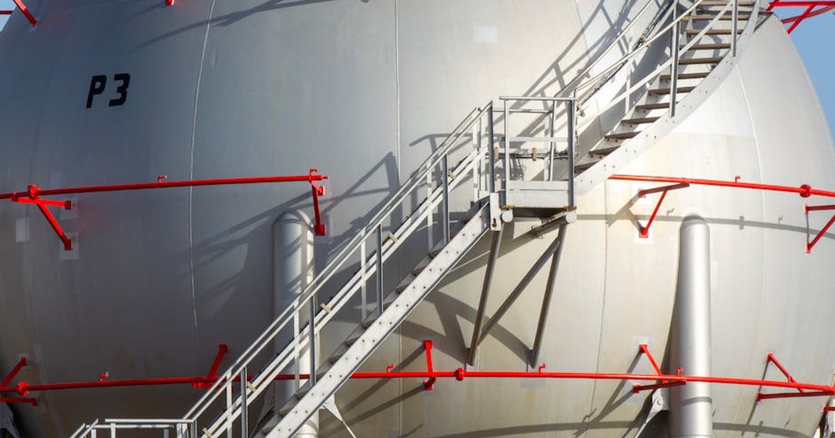Large industrial storage tank with metal staircase and red railings, symbolizing progress.