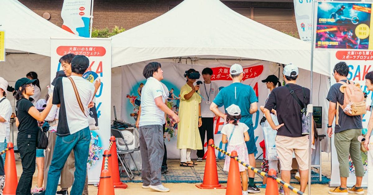 People gather at an outdoor fair booth, enjoying a virtual reality experience in a festive setting.