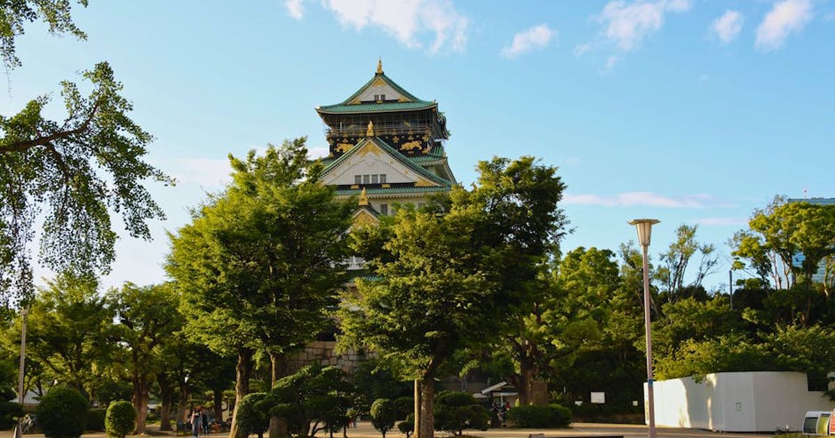 Explore the historic Osaka Castle surrounded by vibrant greenery, set against a clear blue sky.