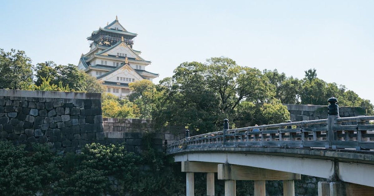 Scenic view of Osaka Castle with a traditional wooden bridge on a sunny day.